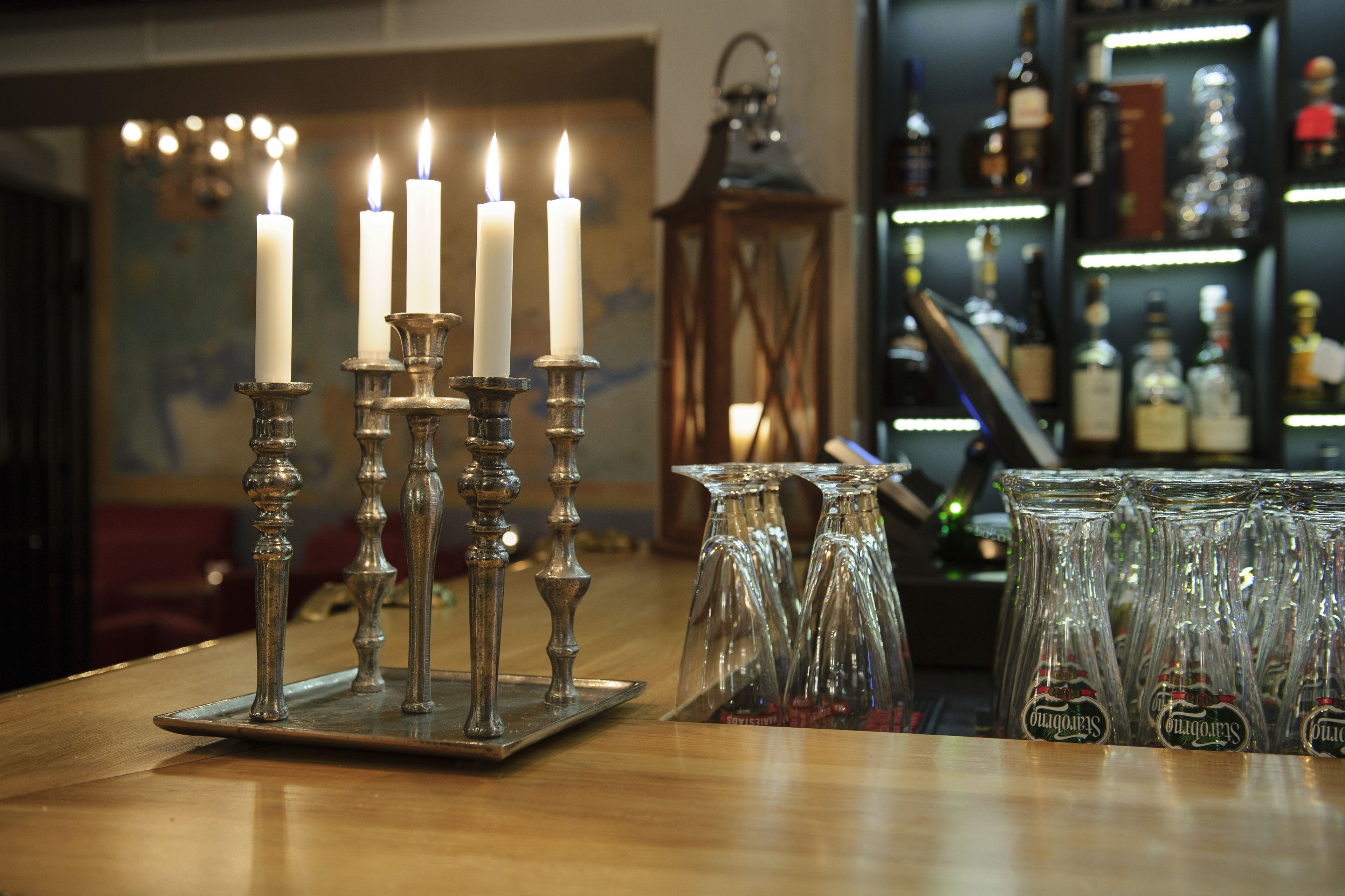 Zona de bar con un candelabro con velas blancas, un farol y una estantería con botellas.