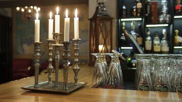 Zona de bar con un candelabro con velas blancas, un farol y una estantería con botellas.