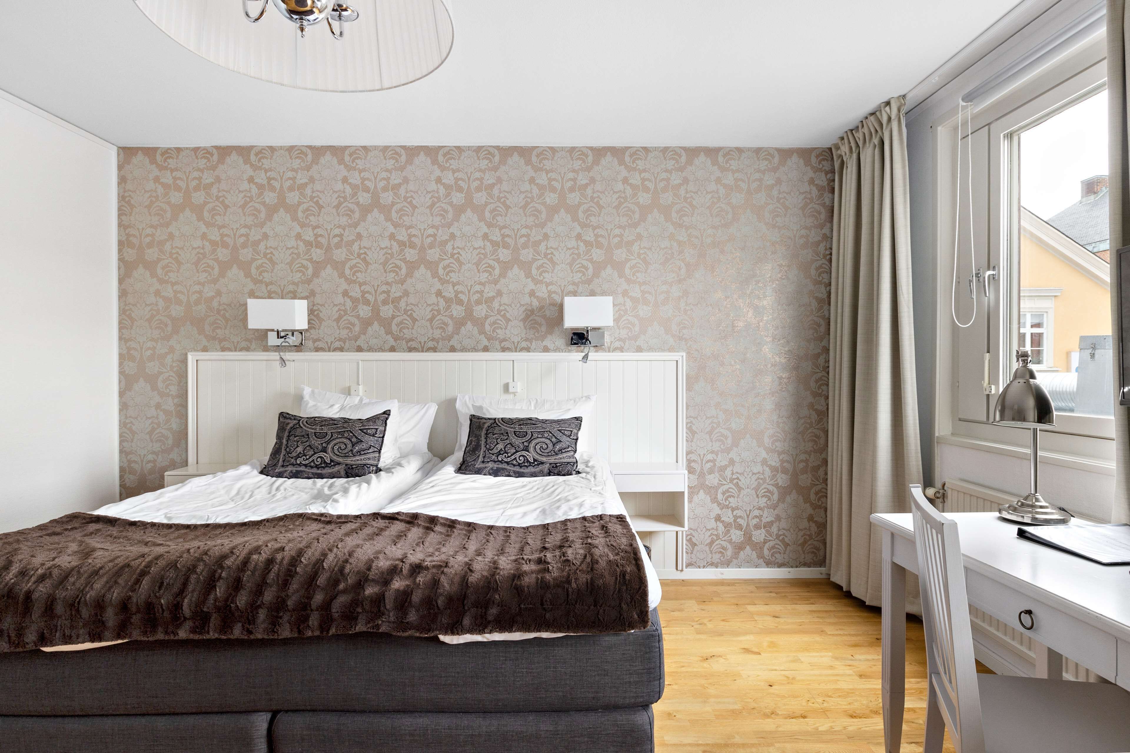A bedroom with a bed, bedside lamps, a desk, and a window with curtains.