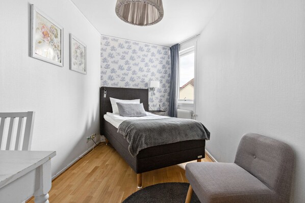 A compact bedroom with a bed, a chair, a table, and a window.