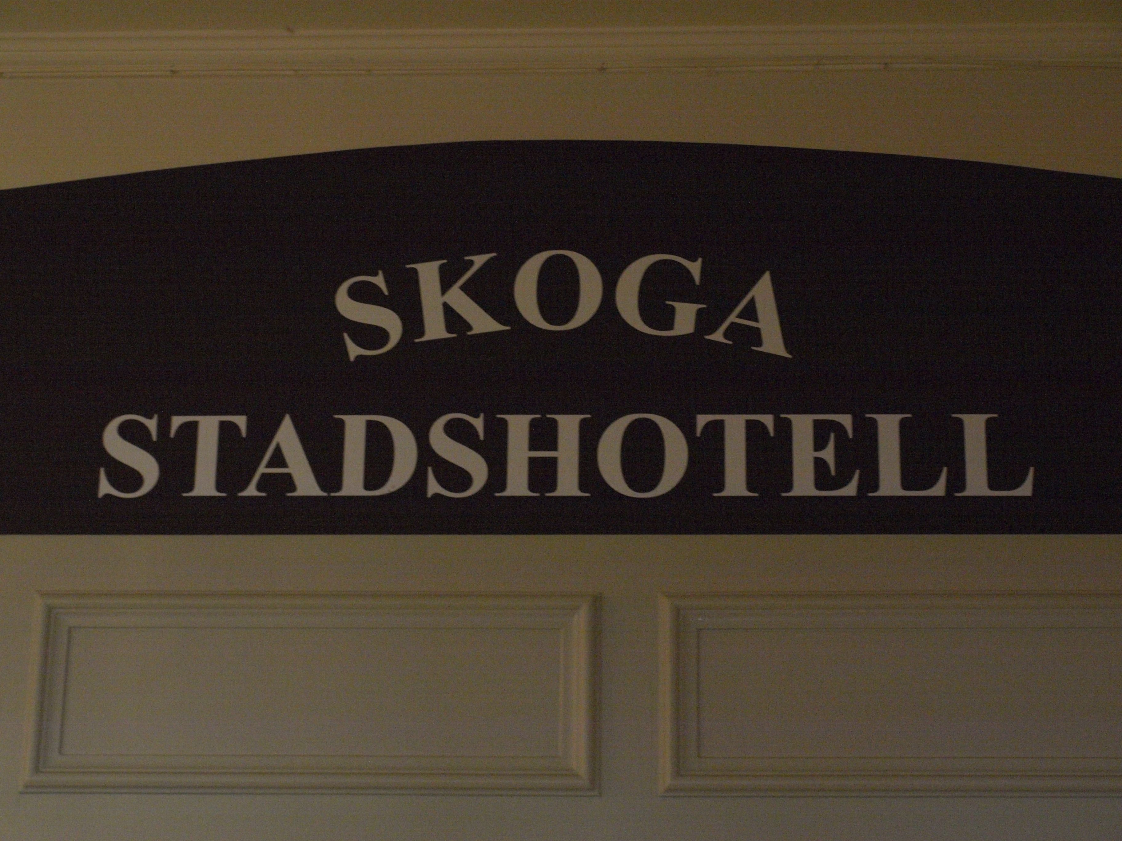 A sign with the text "SKOGA STADSHOTELL".