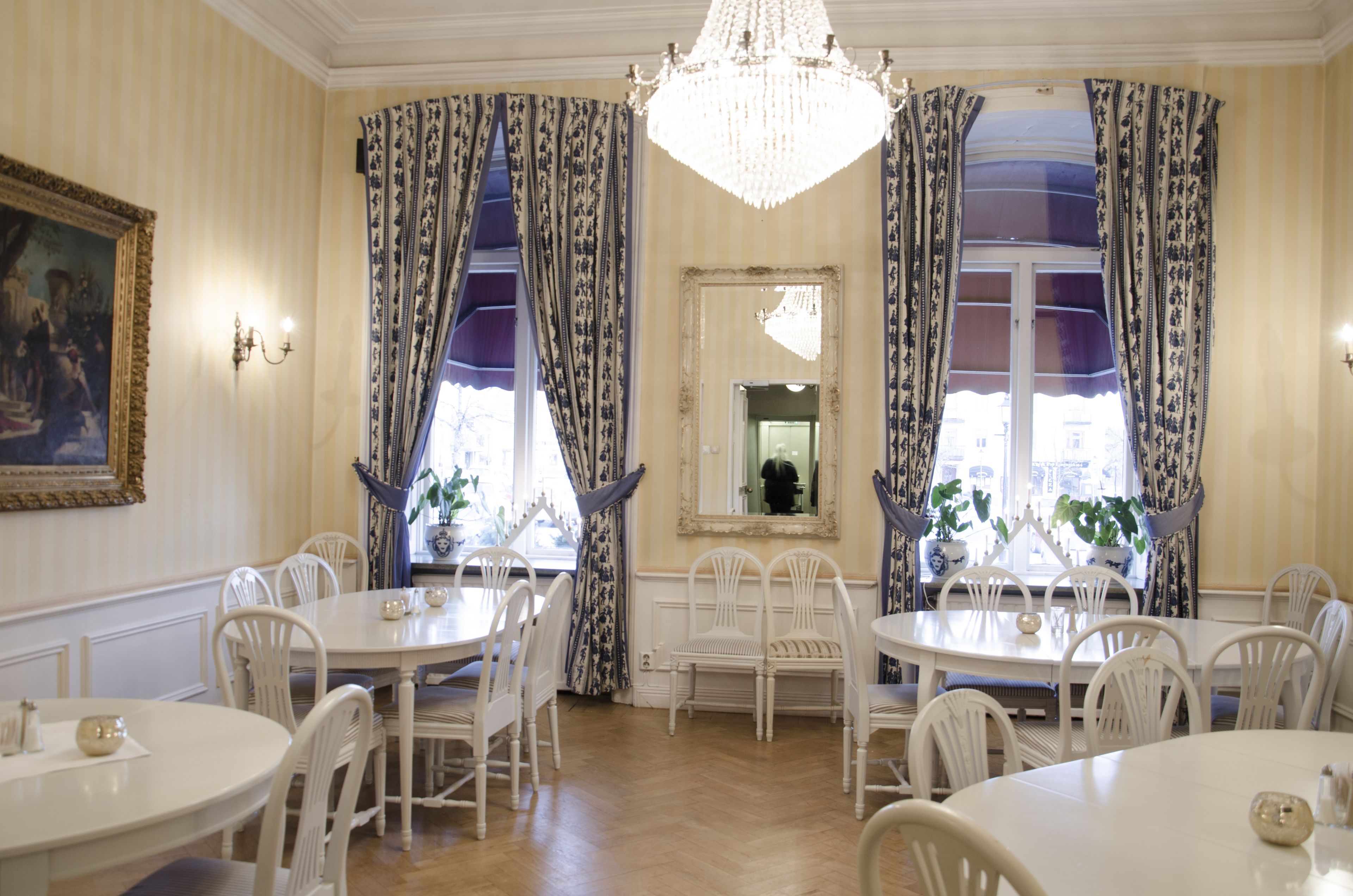 Ein Esszimmer mit weißen Möbeln, einer Chandelüster und gemusterten Vorhängen.