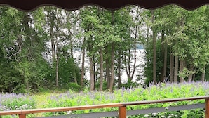 Une terrasse en bois avec une table et des chaises, entourée d’une végétation luxuriante et offrant une vue sur les arbres et les fleurs.