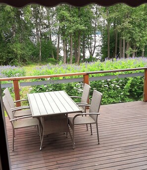 A wooden deck with a table and chairs, surrounded by lush greenery and a view of trees and flowers. - Kiurun Villas (Lappeenranta)