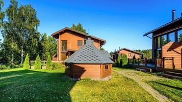 A wooden cabin with a sloped roof, surrounded by a well-maintained lawn and trees.