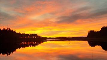 A calm lake reflecting a sunset with a forested shoreline.