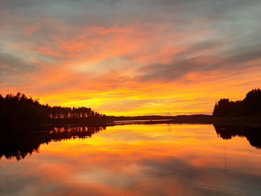 A calm lake reflecting a sunset with a forested shoreline.