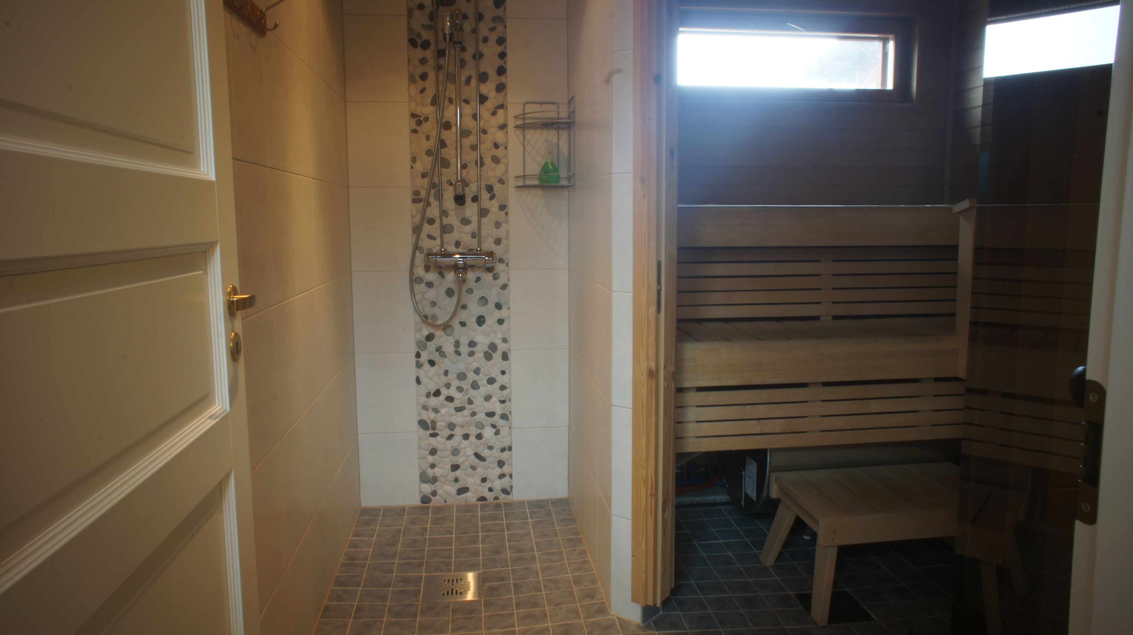 Un baño con ducha, un estante pequeño con artículos de aseo y un banco de madera.