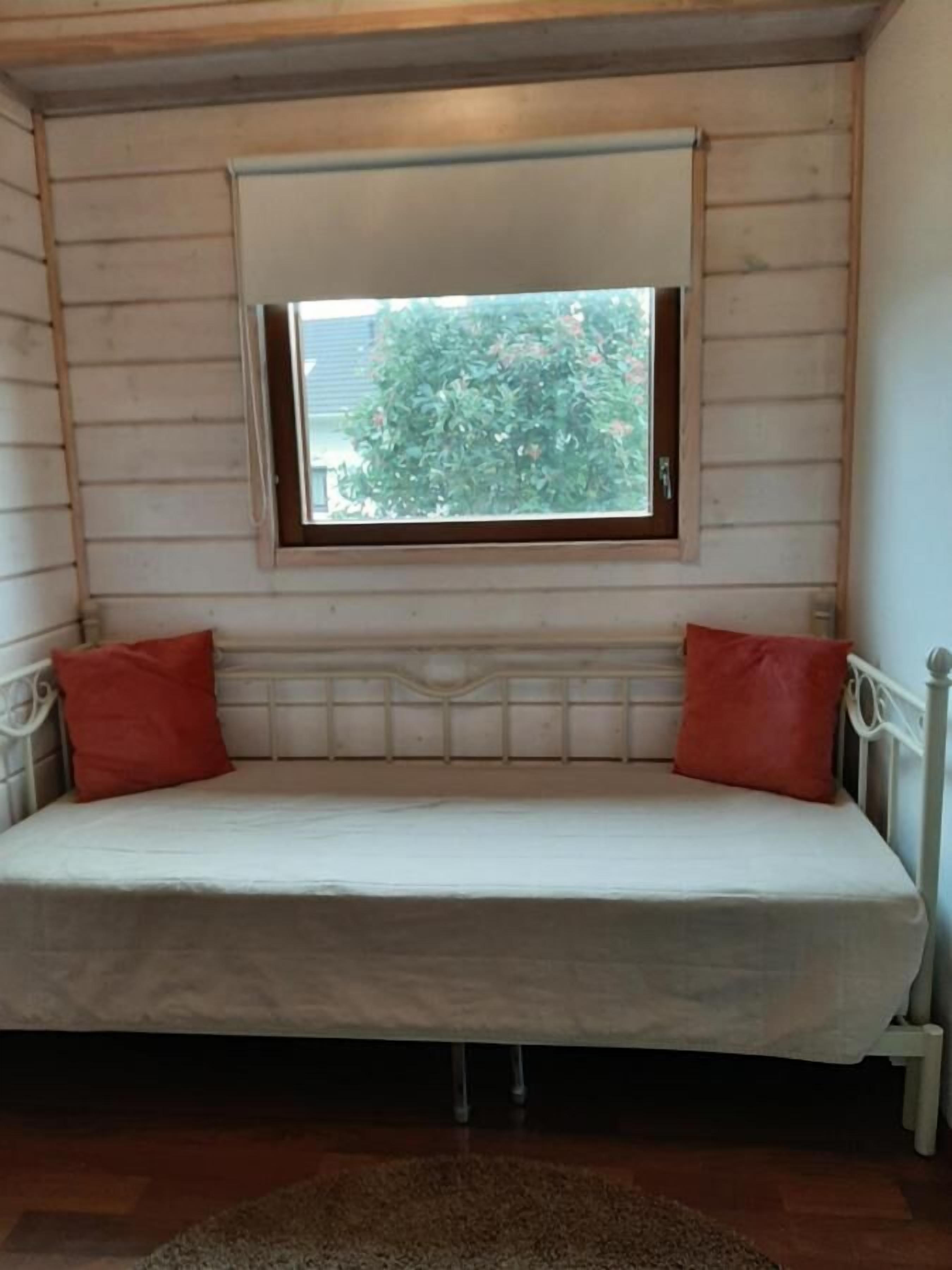 Ein kleiner, gemütlicher Raum mit einem Einzelbett, einem Fenster mit Blick auf Grünflächen und Holzwänden.