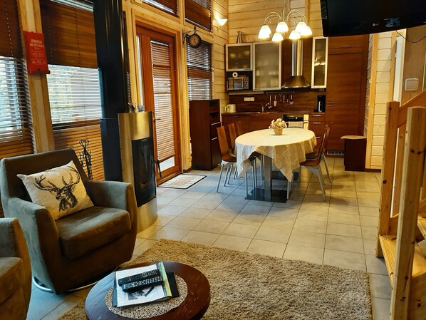 A cozy living room with a fireplace, a dining area with a round table, and a kitchen with wooden cabinets.