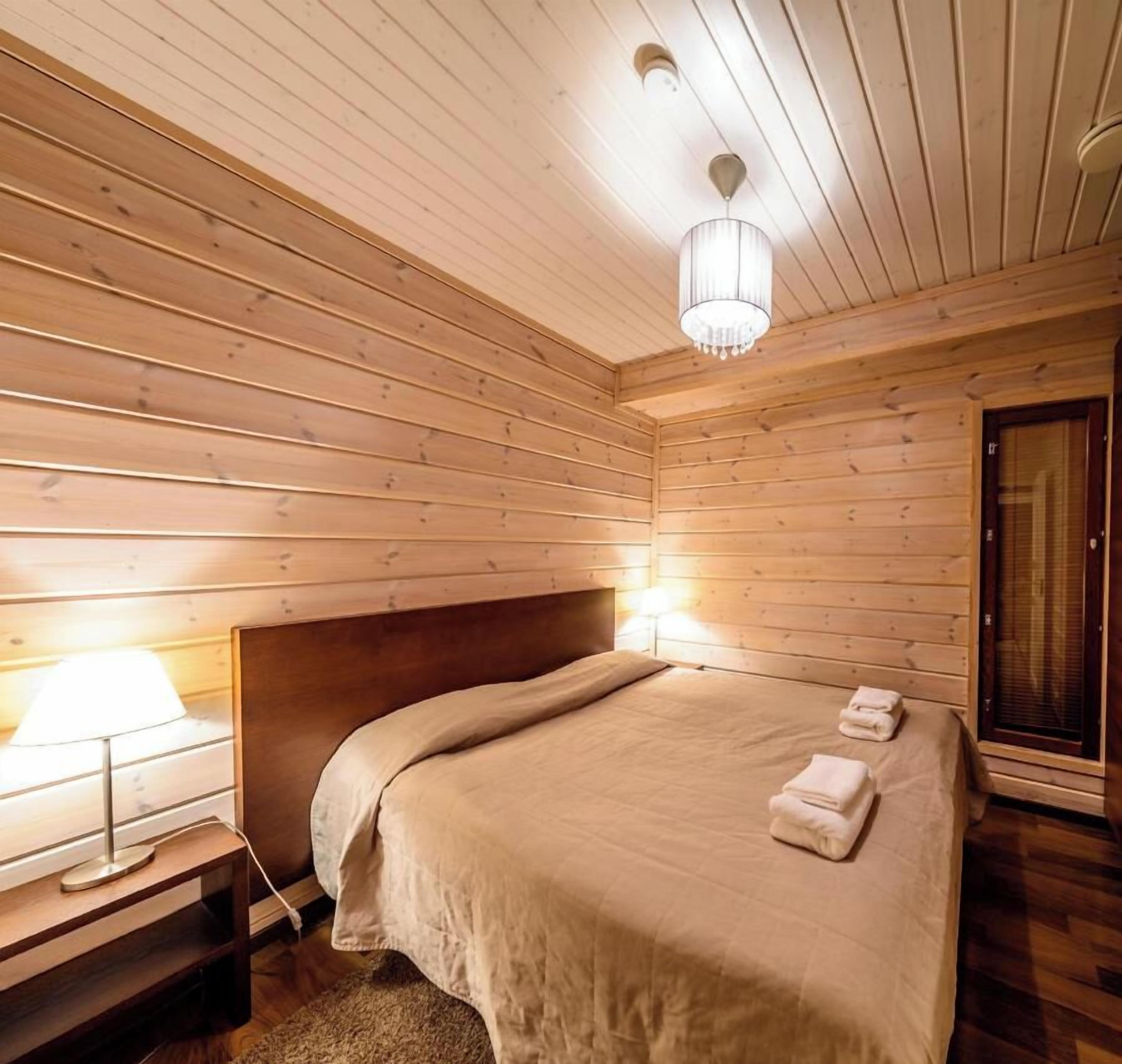 A wooden-paneled room with a bed, bedside lamp, and a door.