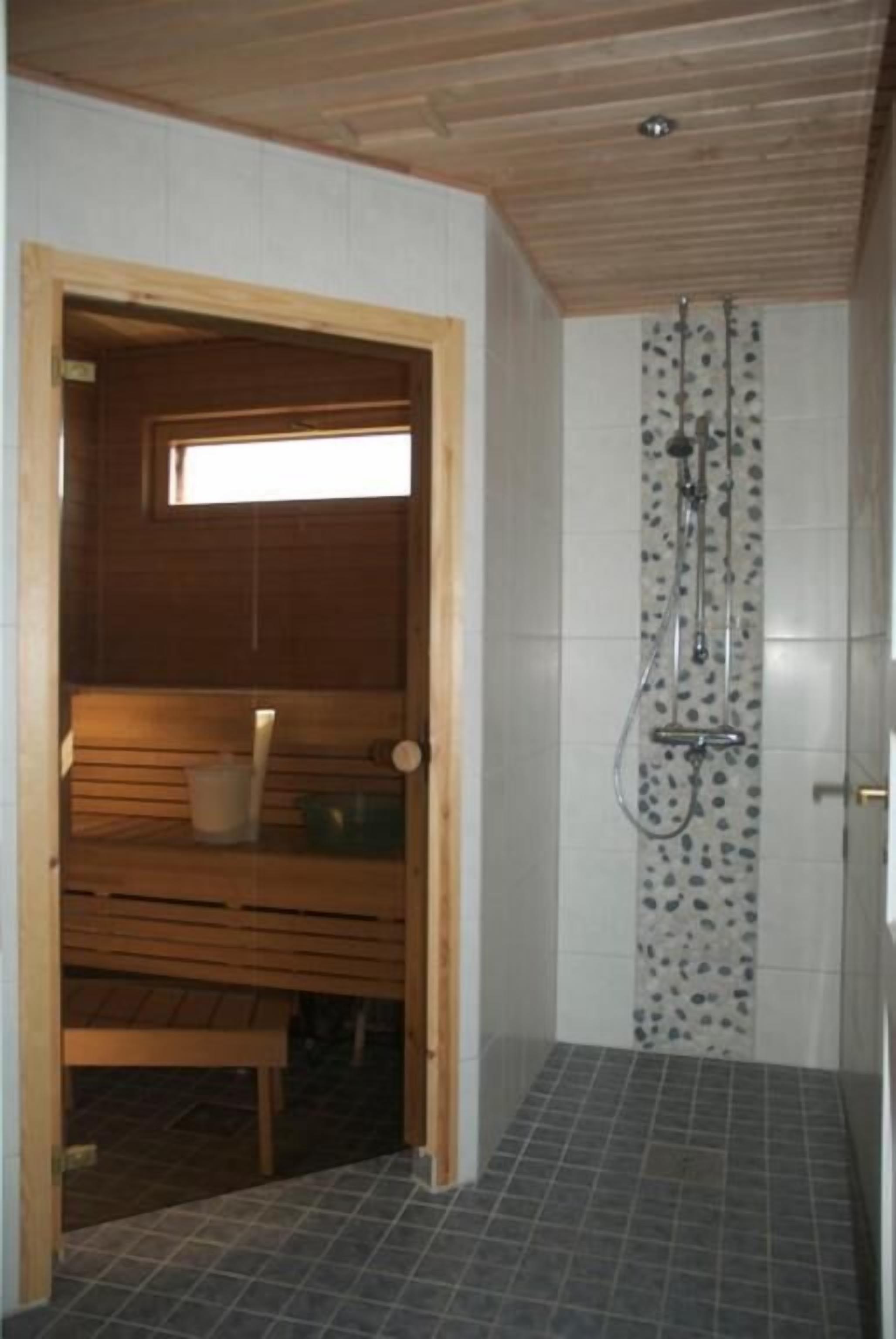 Un sauna avec un banc en bois, une petite fenêtre et un espace douche avec un mur carrelé.