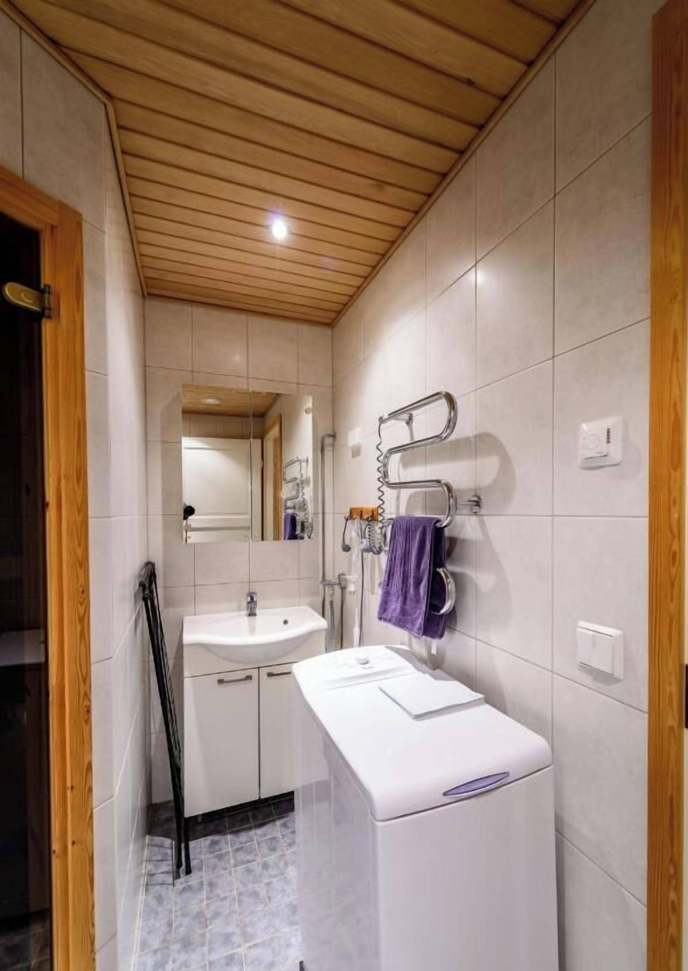 A bathroom with a wooden ceiling, white tiles, a sink, a mirror, and a towel rack.