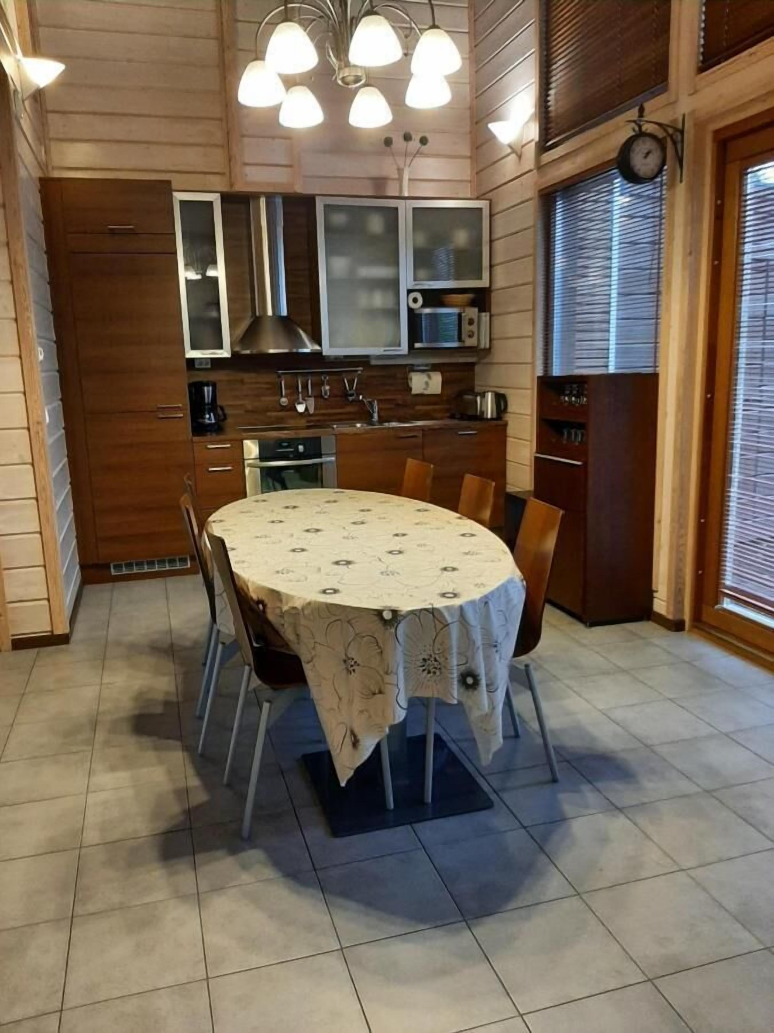 A dining area with a round table, chairs, a clock, and a kitchen in the background.