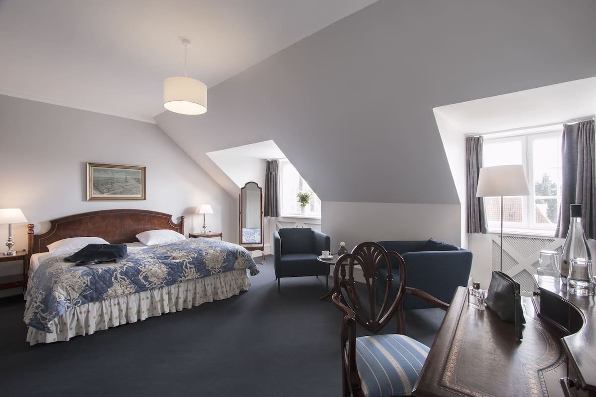 A hotel room with a bed, a desk, a chair, a sofa, and a window.