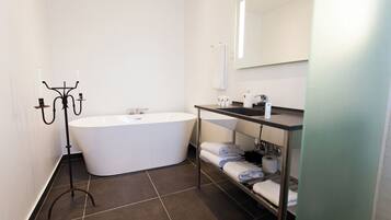 A modern bathroom with a freestanding bathtub, a vanity with a mirror, and shelves for towels.