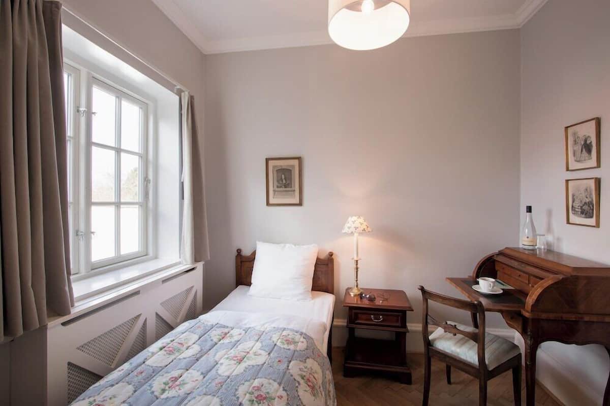 A bedroom with a bed, a desk, a chair, a lamp, and a window with curtains.