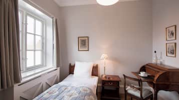 Une chambre à coucher avec un lit, un bureau, une chaise, une lampe et une fenêtre avec des rideaux.