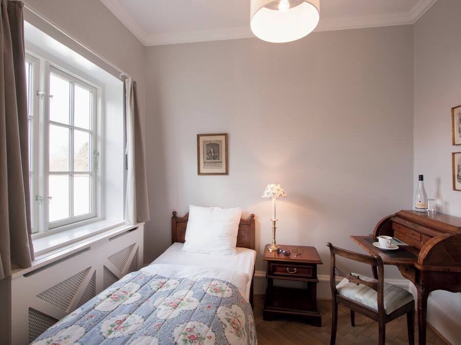 Une chambre à coucher avec un lit, un bureau, une chaise, une lampe et une fenêtre avec des rideaux.