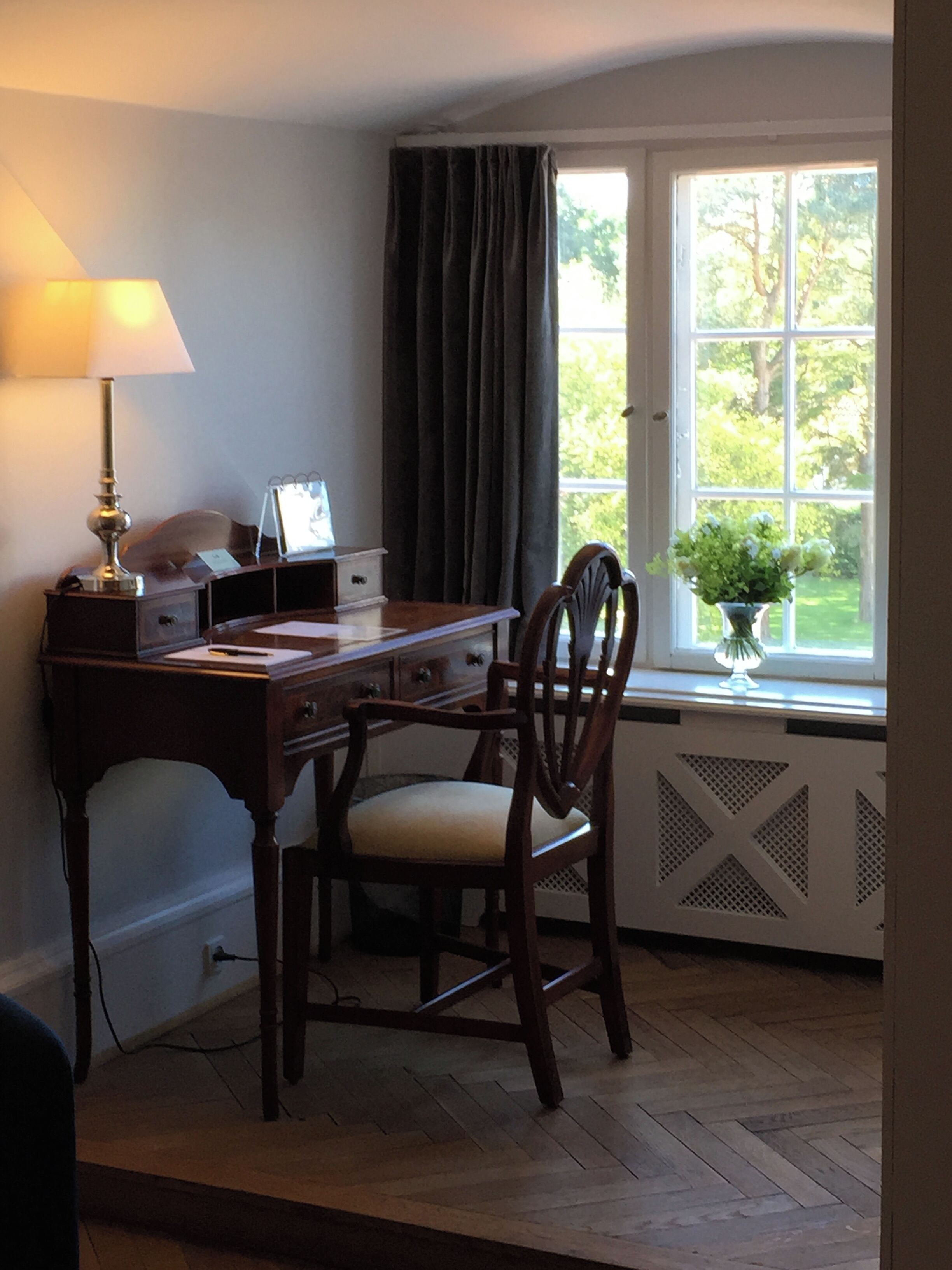 A study room with a desk, chair, lamp, and a window with curtains.