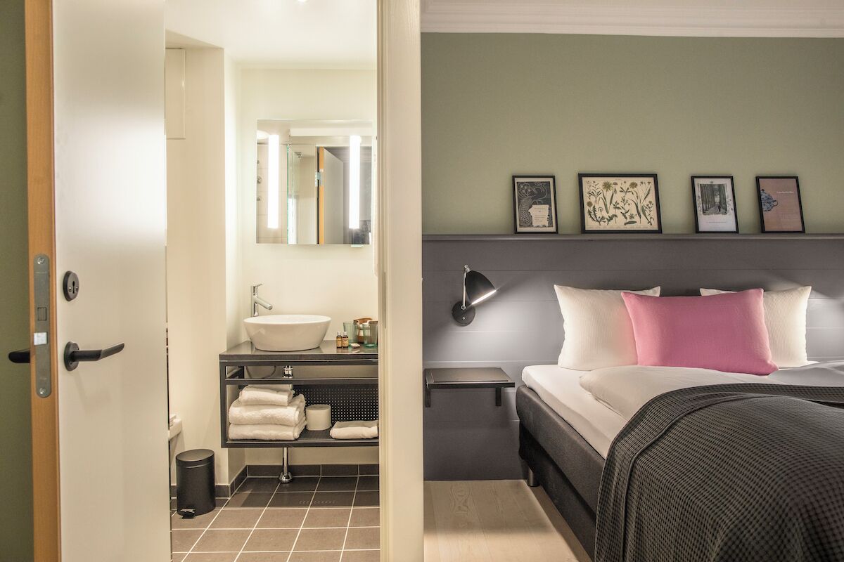 A hotel room with a bed, bedside table, and a bathroom with a sink and mirror.