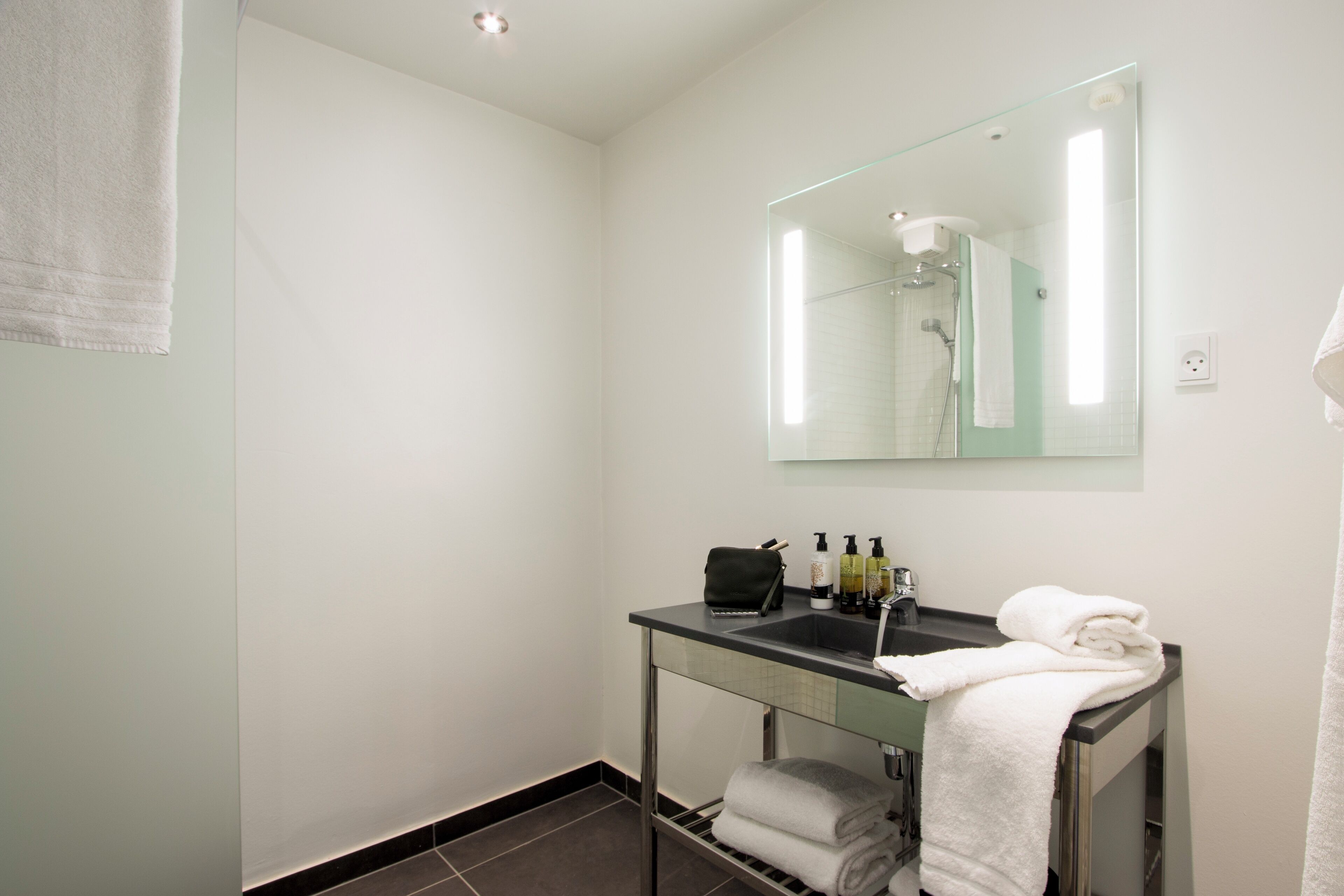 Une salle de bain moderne avec un meuble-lavabo en verre, un miroir, un porte-serviettes et un espace douche.
