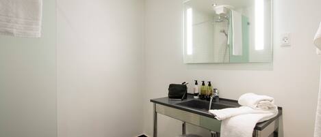 A modern bathroom with a glass vanity, a mirror, a towel rack, and a shower area.