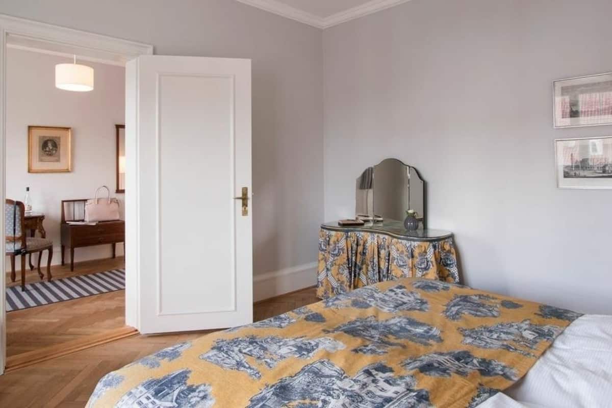 A bedroom with a bed, a dresser, a mirror, and a door leading to another room.