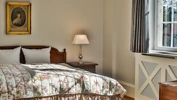 A bedroom with a wooden bed, a nightstand with a lamp, a framed portrait on the wall, and a window with curtains.