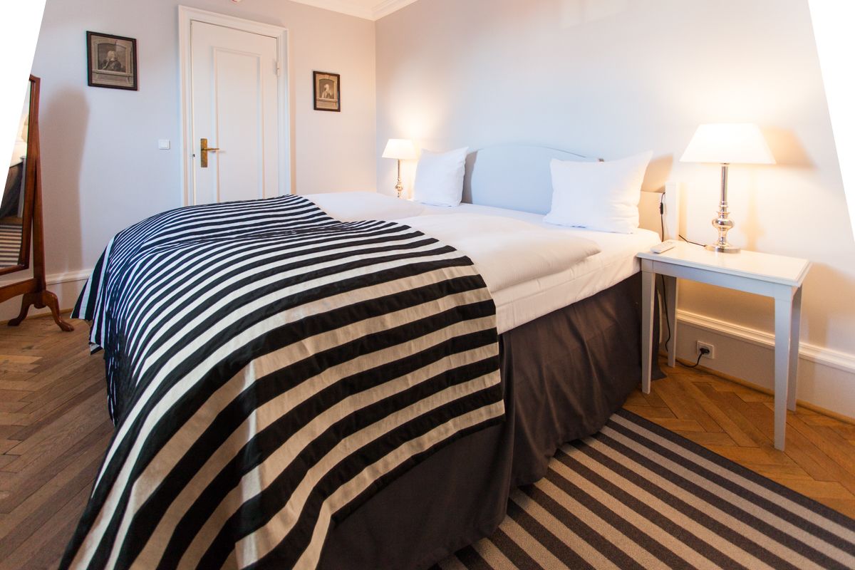 Una habitación de hotel con una cama grande, dos mesitas de noche con lámparas, piso de madera y una alfombra a rayas.