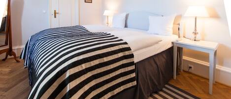 Una habitación de hotel con una cama grande, dos mesitas de noche con lámparas, piso de madera y una alfombra a rayas.