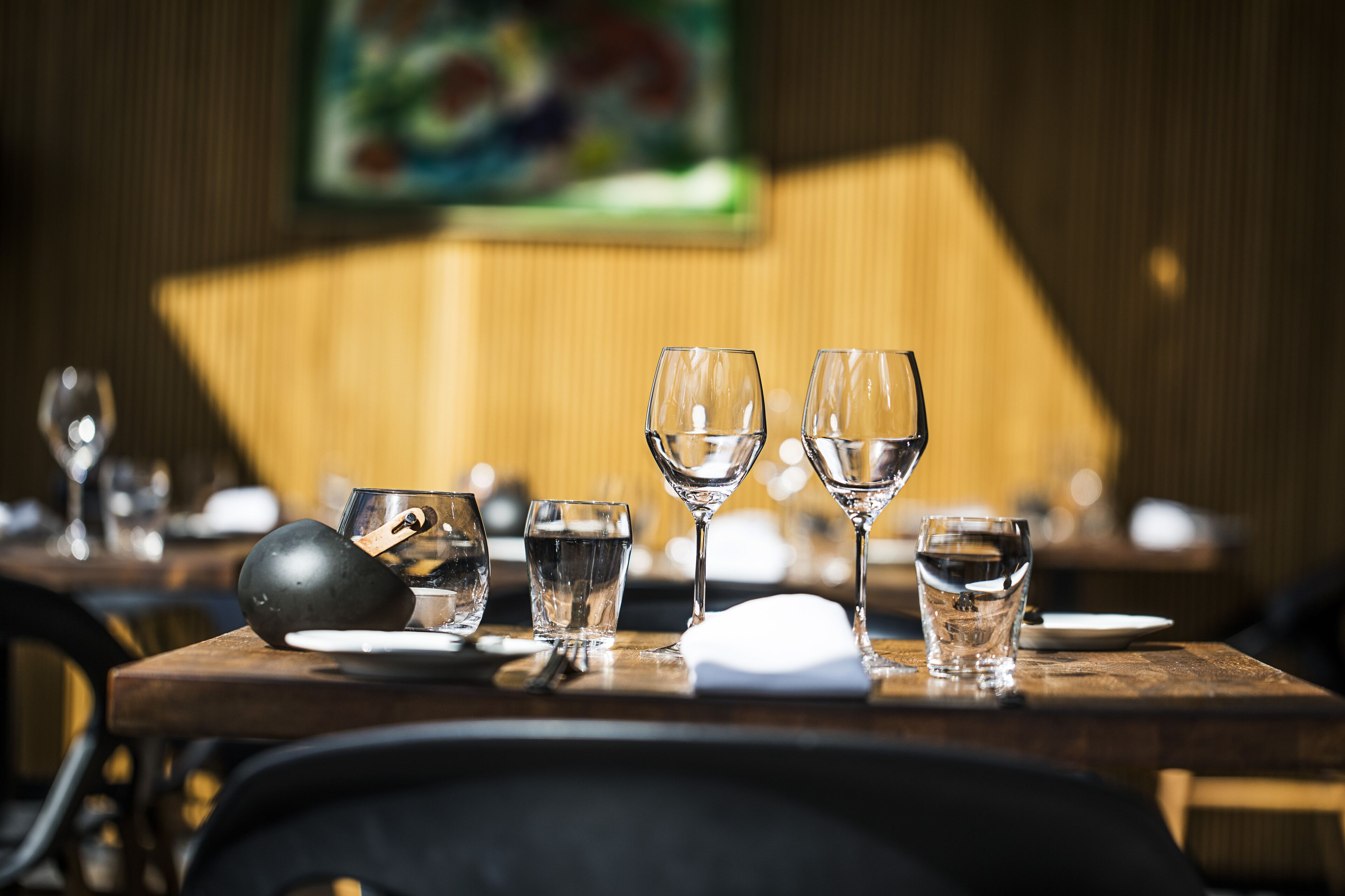 A dining table with various glassware and plates, set in a restaurant with a wooden interior and a painting on the wall.