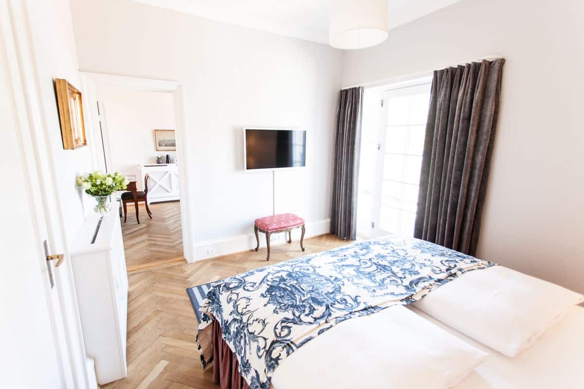 A hotel room with a bed, a TV, a small table with a plant, and a view of the outside.