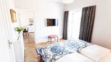 A hotel room with a bed, a TV, a small table with a plant, and a view of the outside.