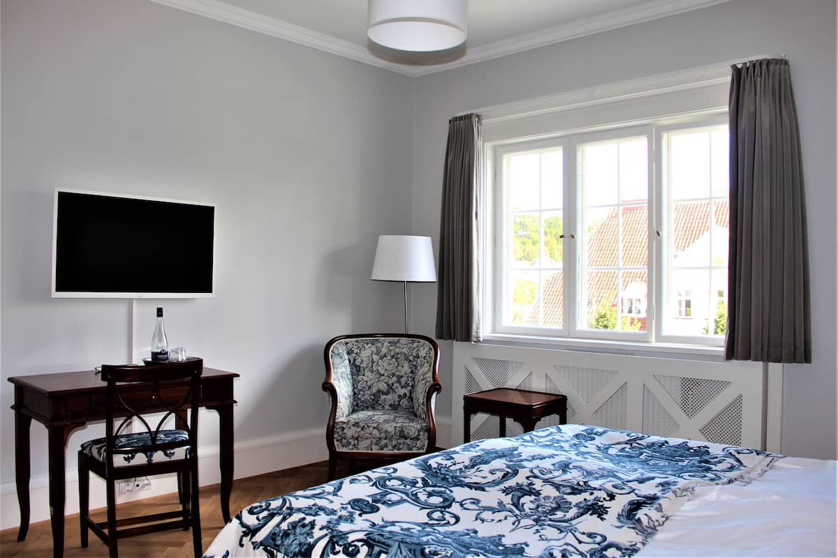 A hotel room with a bed, a desk, a chair, a TV, and a window with curtains.