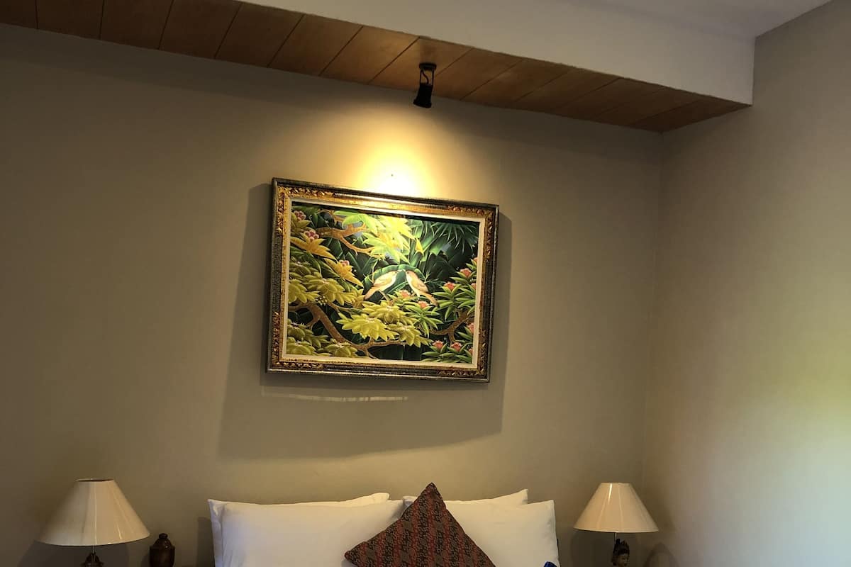 A hotel room with a bed, two bedside tables with lamps, a painting on the wall, and a ceiling light.