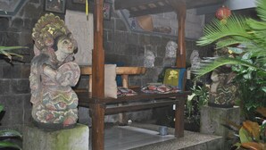 A traditional room with a stone wall, a wooden bench, and a statue. - Jangkrik Homestay (Ubud)