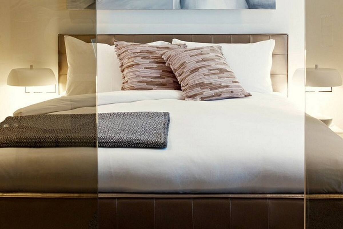 A modern hotel bedroom with a large bed, two bedside lamps, and a large abstract painting above the bed.