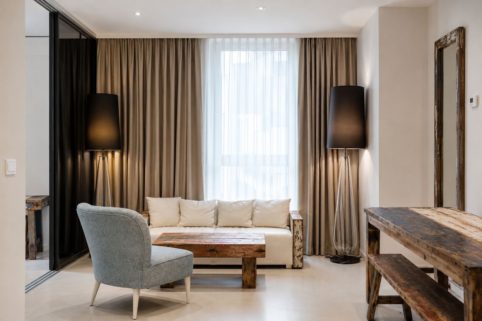 A modern living room with a sofa, a coffee table, a chair, and a wooden bench. There are two floor lamps and a large mirror on the wall.