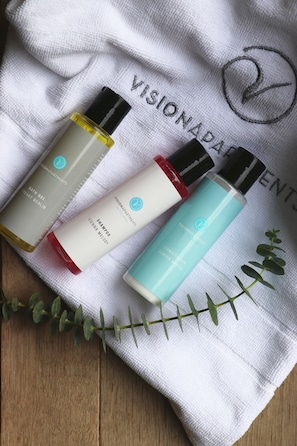 Three bottles of skincare products on a white towel with the text "VISIONNADAPTENTS". - VISIONAPARTMENTS Berlin Otto-Braun-Strasse (Berlin)
