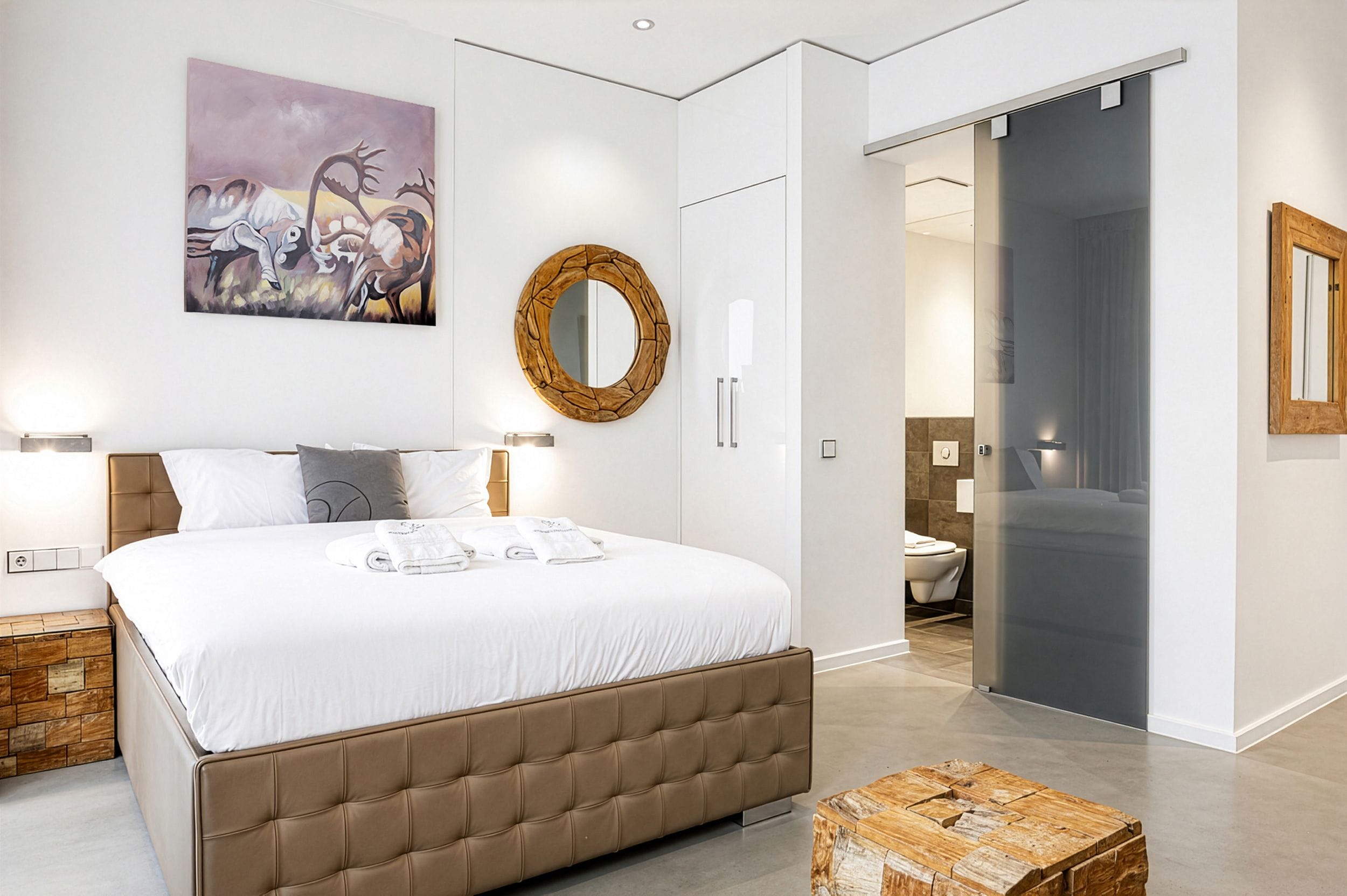Une chambre à coucher moderne avec un grand lit, un miroir à cadre en bois et un tableau accroché au mur.