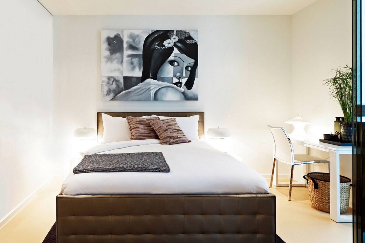 A modern bedroom with a large bed, a desk with a chair, and a wall-mounted painting.