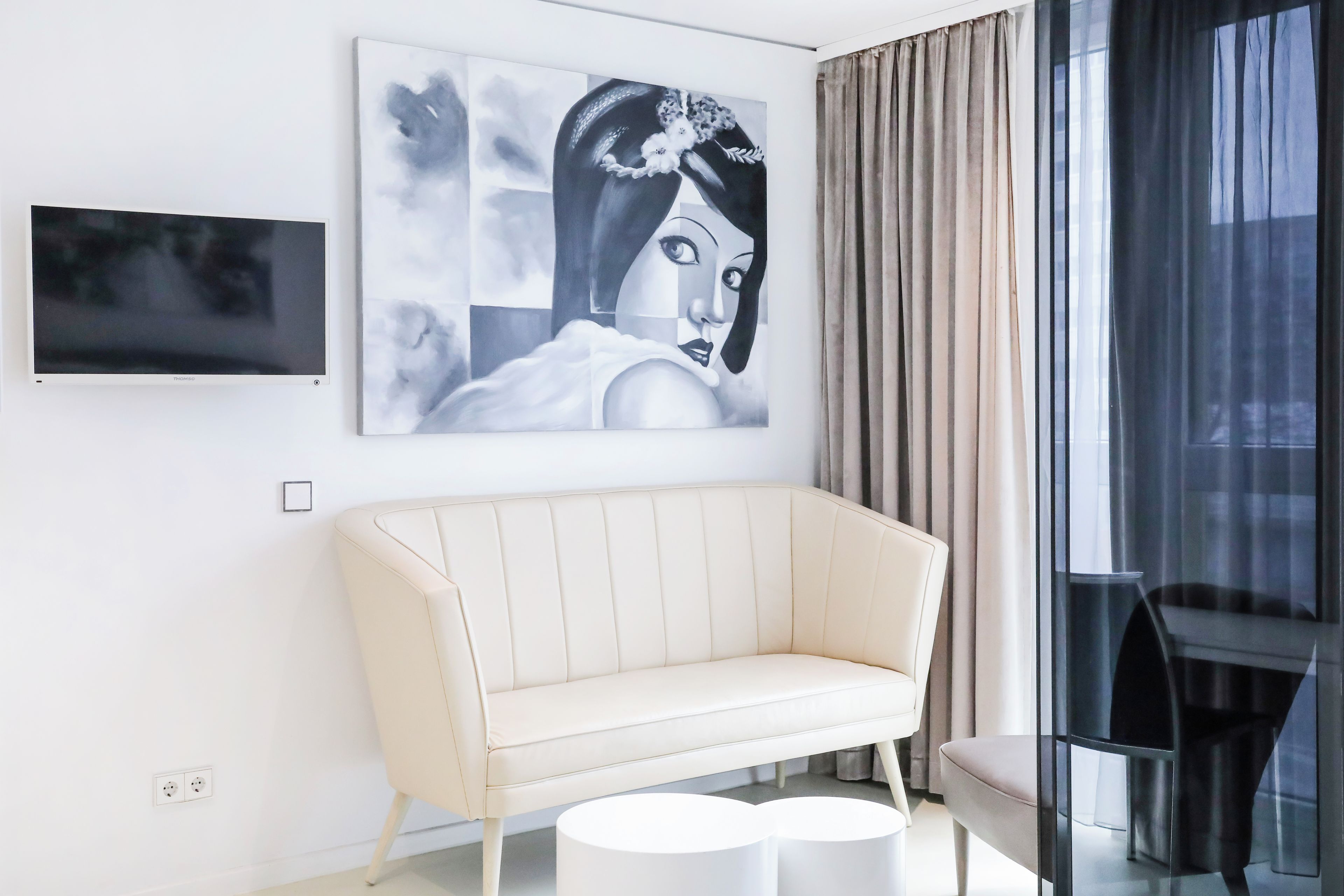 Een moderne woonkamer met een witte bank, een ronde salontafel, een flatscreen televisie en een groot abstract schilderij.