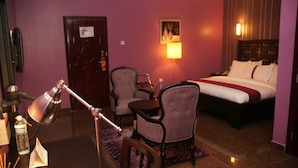 A hotel room with a bed, two armchairs, a desk with a lamp, a door, and a wall-mounted light. - Ellis Suites Limited (Lagos)