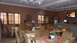A dining area with tables set for four, each with a vase of flowers and a candle. There are multiple tables and chairs arranged in the room. - Ellis Suites Limited (Lagos)