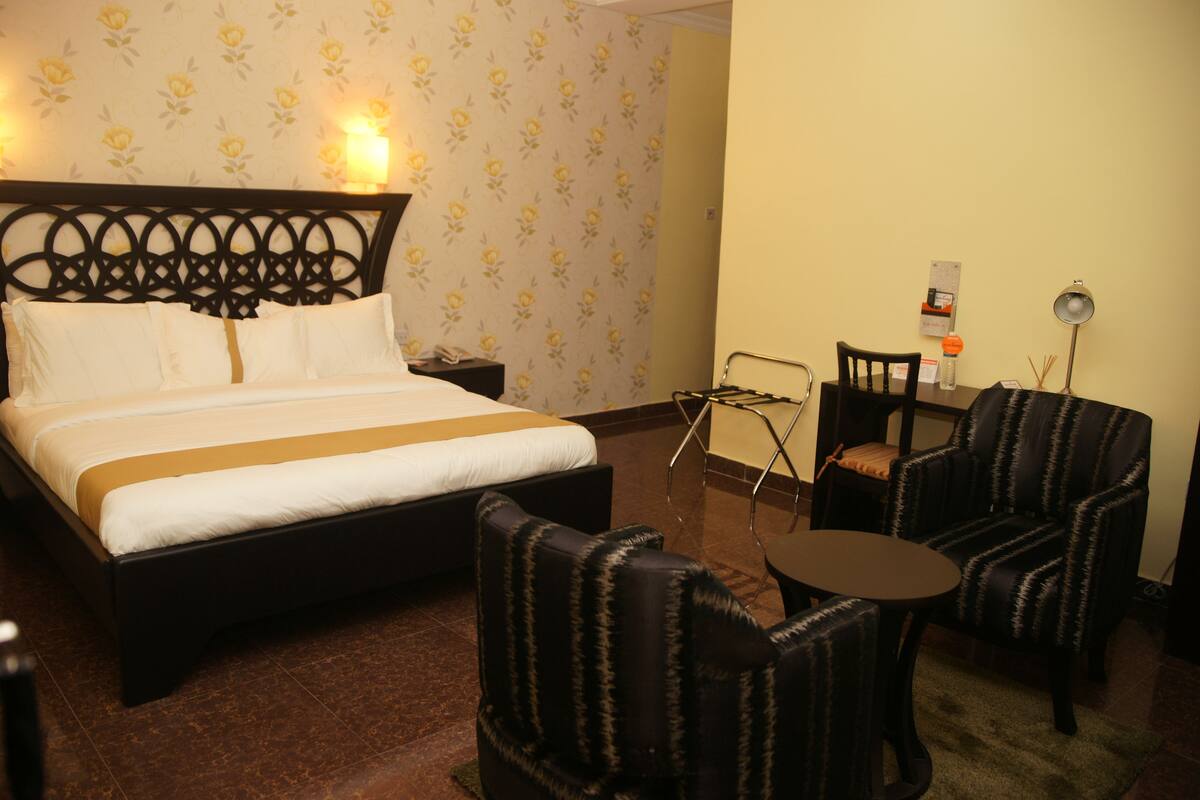 A hotel room with a bed, two armchairs, a small table, a nightstand, and a lamp.