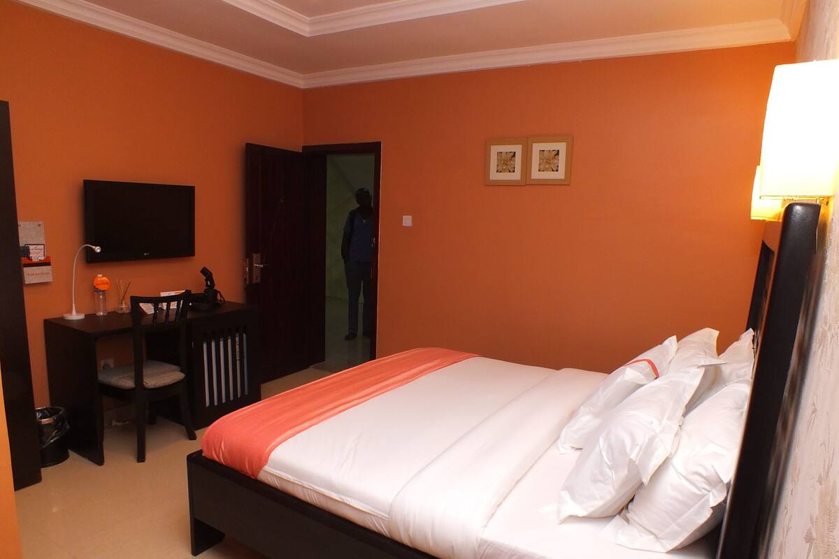A hotel room with a bed, a desk, a chair, a television, and two framed pictures on the wall.