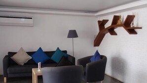 A modern living room with a dark sofa, two armchairs, and a coffee table. There is a floor lamp and a unique wooden shelf unit on the wall. - I Room Hotel (Surat Thani)