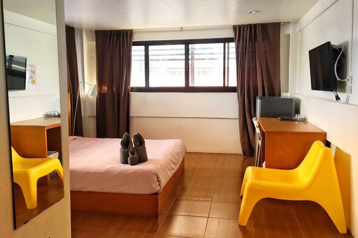 Ett hotellrum med en säng, ett skrivbord, en stol, en tv och ett fönster med gardiner.