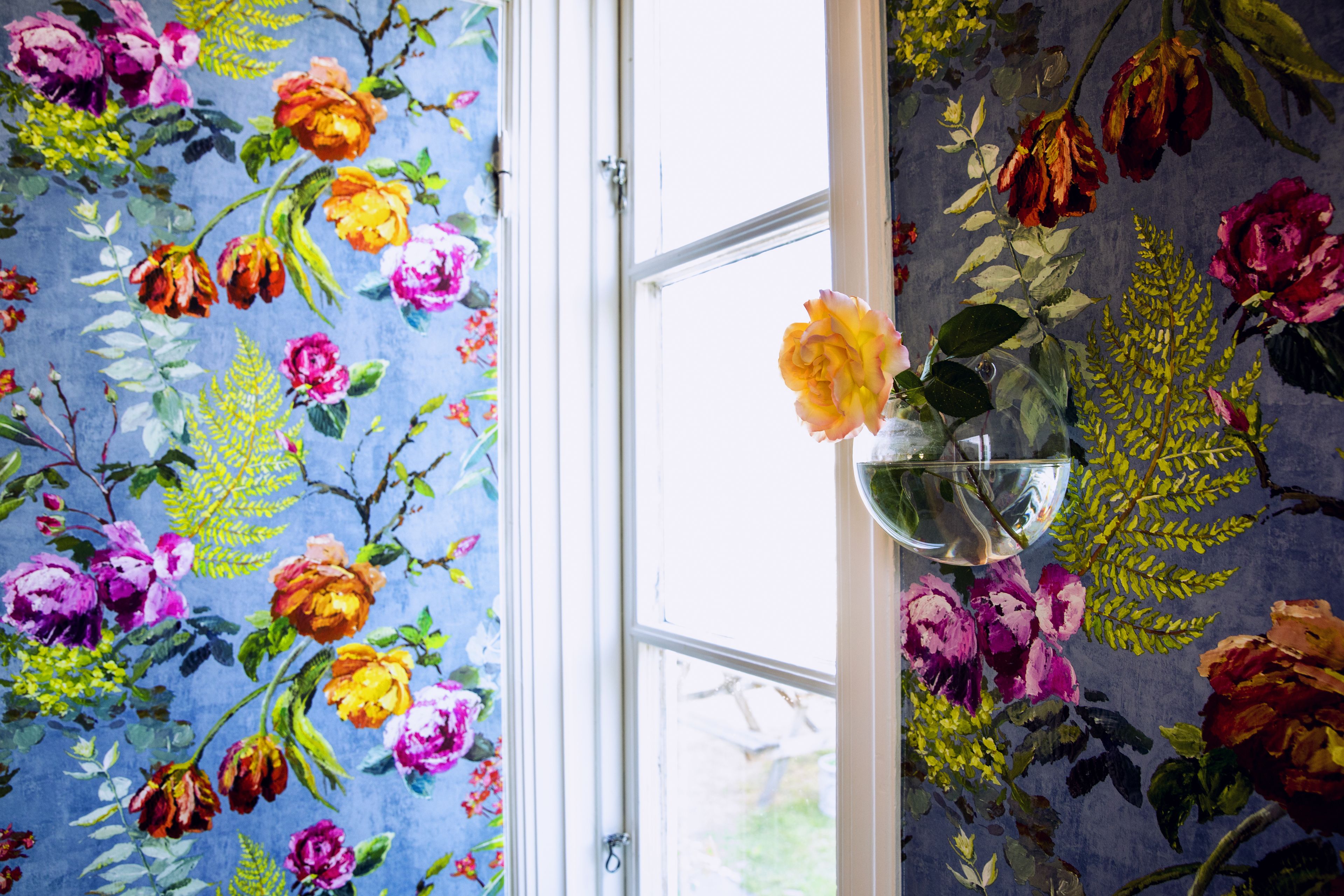 A room with floral wallpaper, a window, and a vase with flowers.
